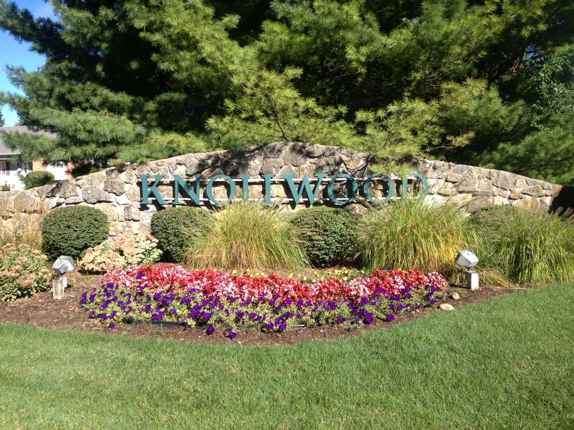 A sign that says knollwood in front of some bushes and flowers.
