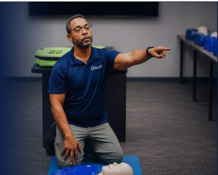 BCEP instructor kneeling beside a CPR training manikin during a hands-on class