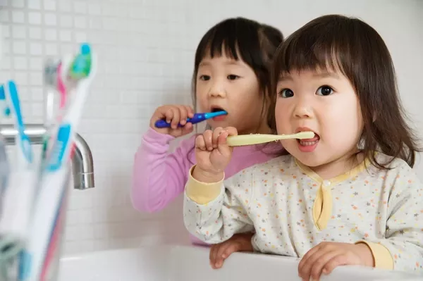 two girl toddlers brushing teeth at bathroom sink